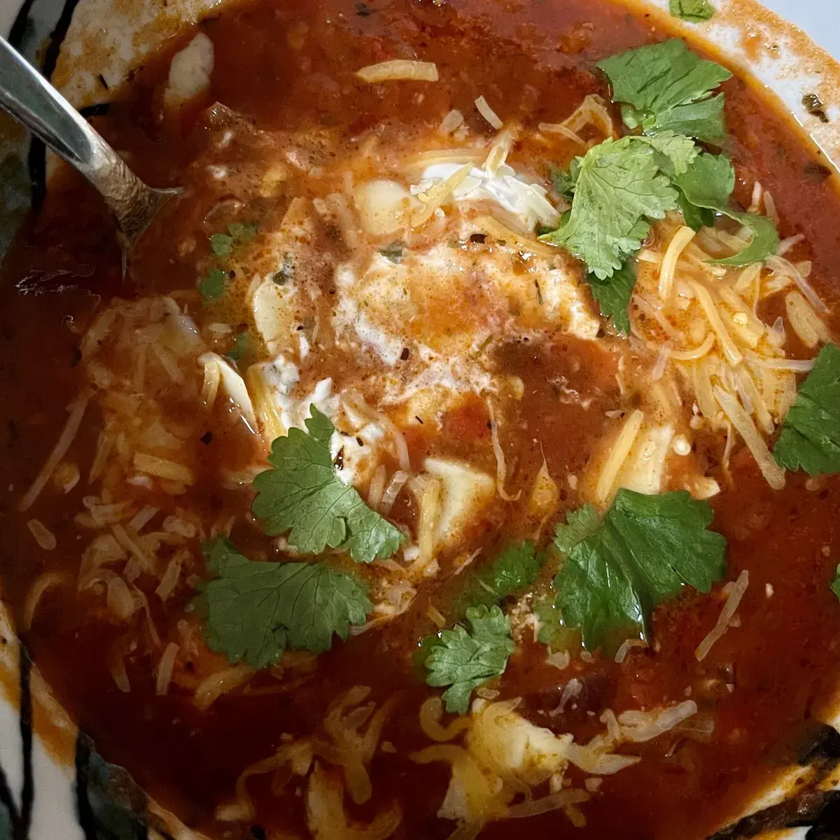 Eine Tomatensuppe mit Käse, Schmand und Korianderblättern.