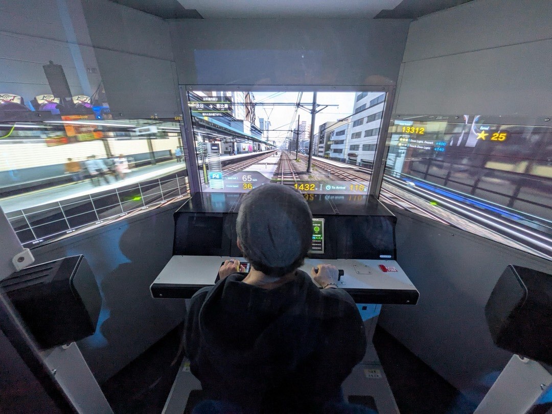 Ich in der Densha de Go! Kabine vor drei Monitoren beim Training für die Umschulung in der zweiten Lebenshälfte.