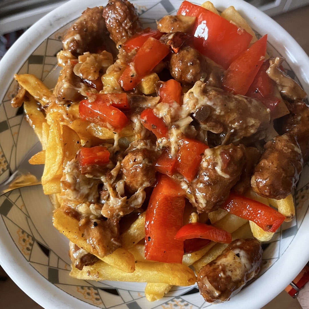 Ein Teller Poutine mit Pommes und roter Paprika.