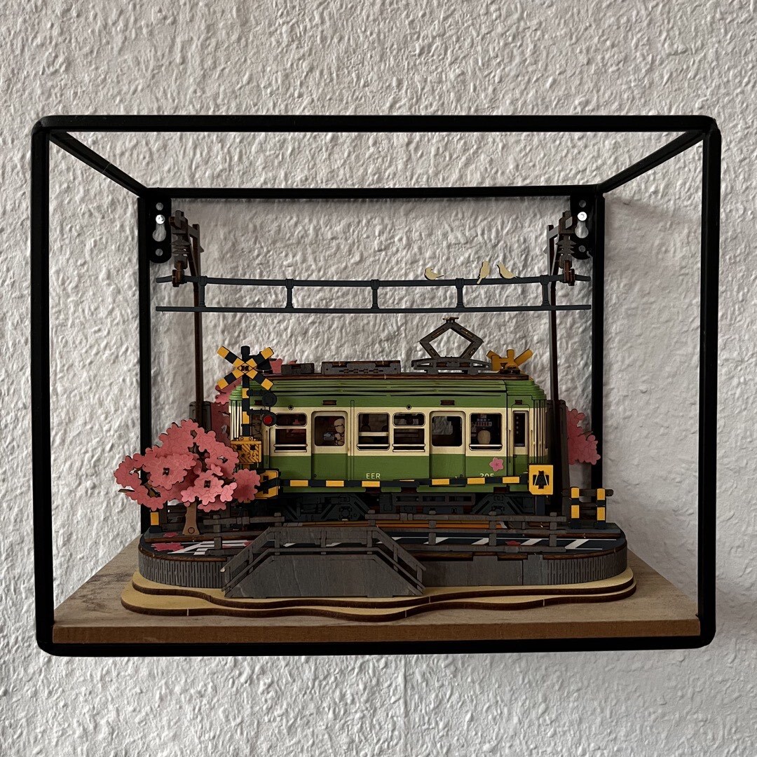 Eine Eisenbahn an einem Bahnübergang mit viel Kirschblüte. Alles aus Holz.