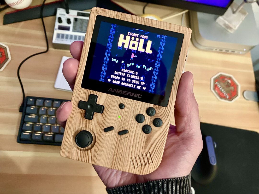 Ein Anbernic Handheld der mit einer Hand in die Kamera gehalten wird. Darauf läuft das Spiel Escape from Höll.
