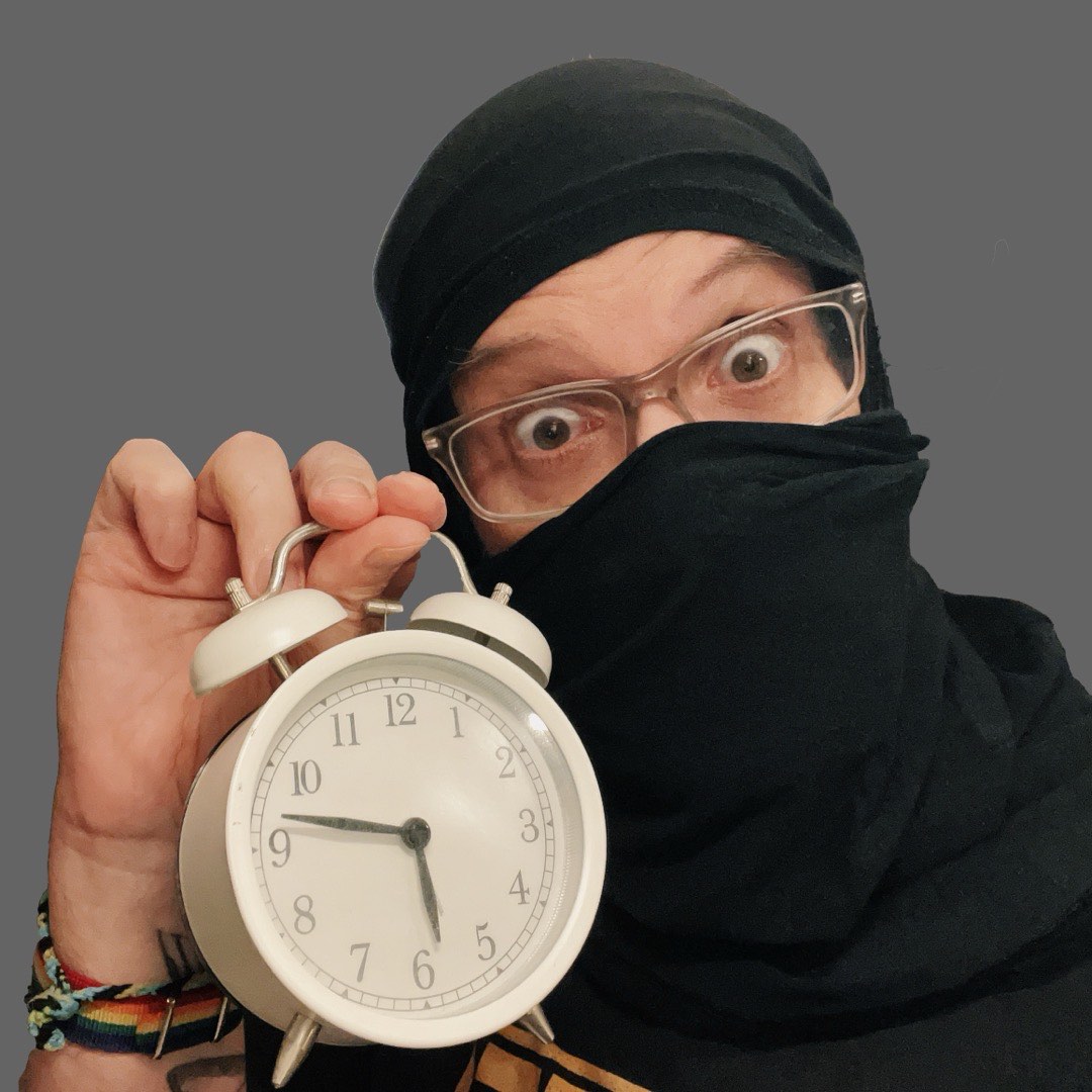 Eine Person (ich) mit einem als Ninja-Maske um den Kopf gewickelten T-Shirt und einem Wecker in der Hand.