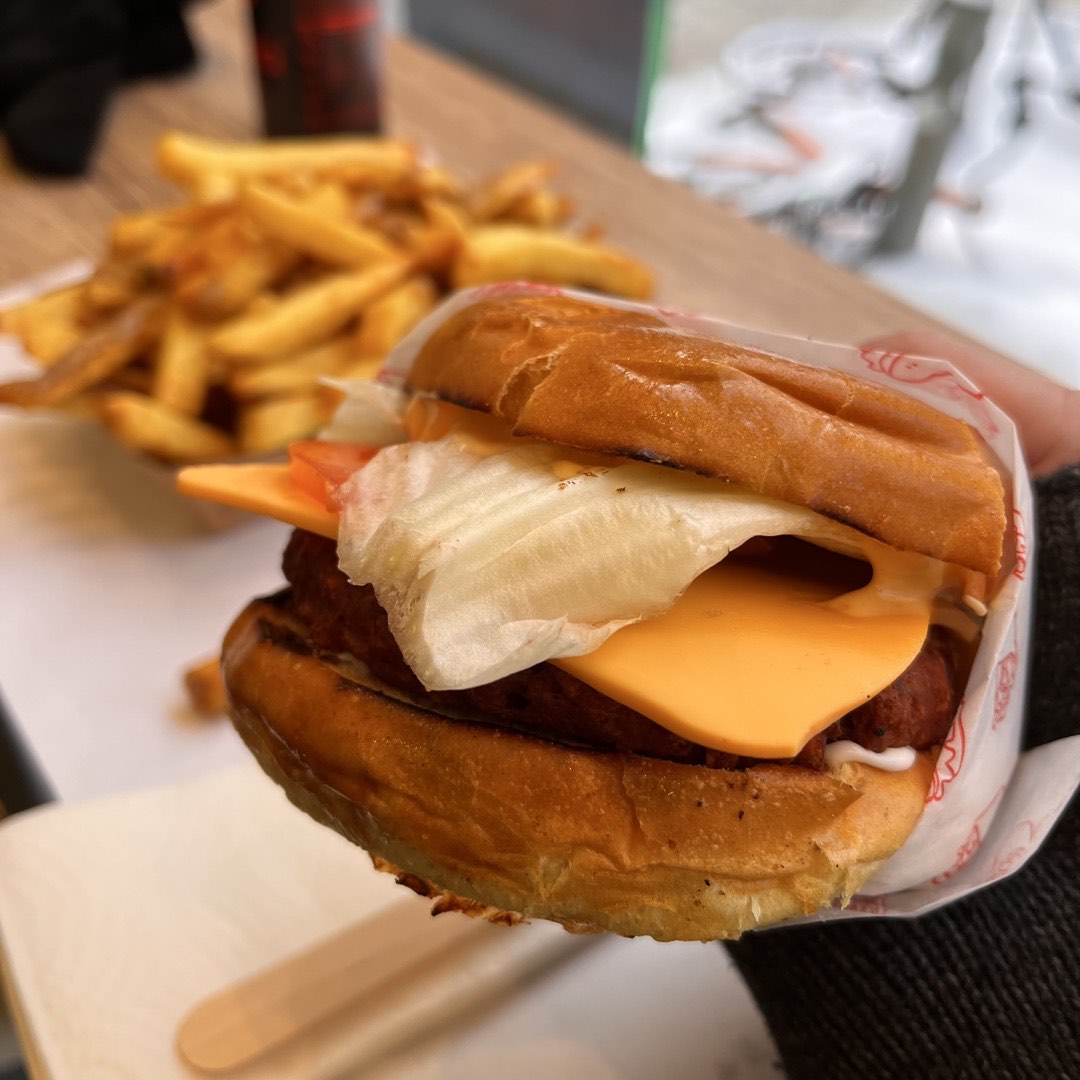 Ein Burger mit einem viel zu großen Salatblatt. Im Hintergrund sind Pommes zu erkennen.
