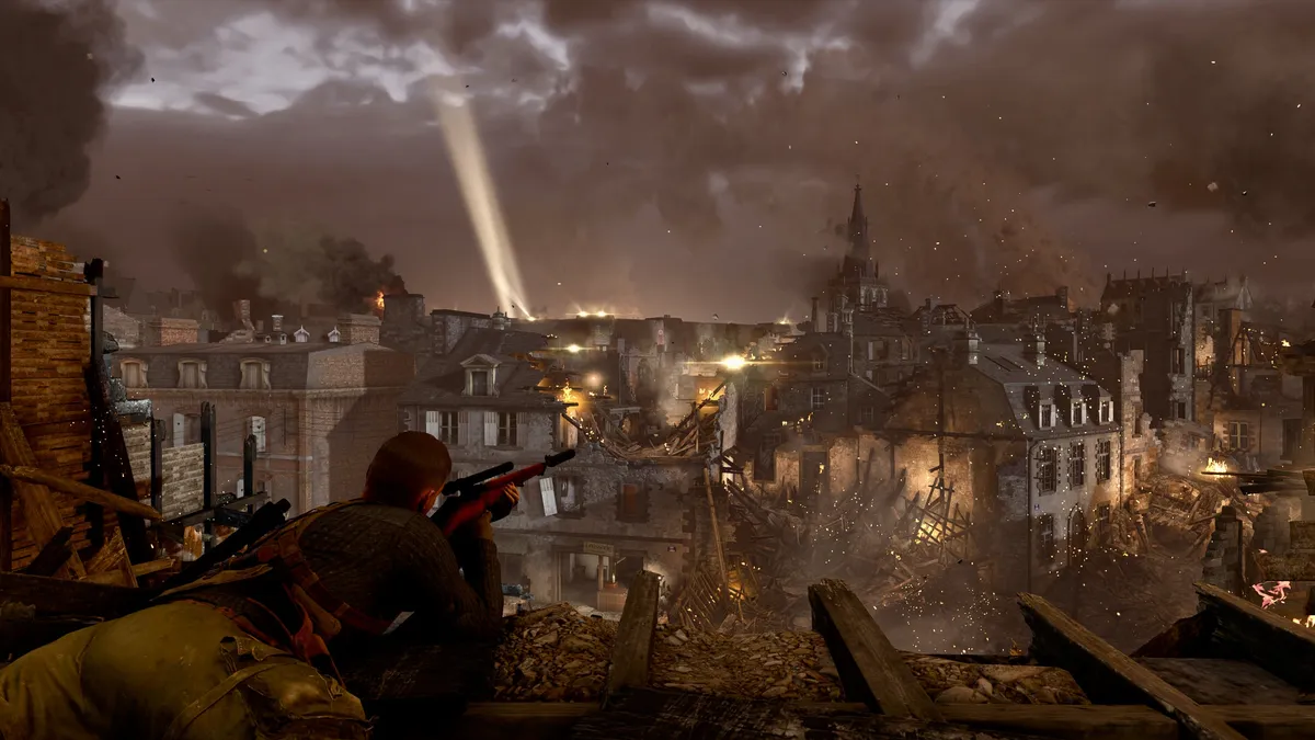 Ein Scharfschütze liegt mit angelegtem Gewehr in einer Hausruine und blickt über die Dächer einer zerbombten und brennenden Stadt. In der Ferne leuchtet ein riesiger Scheinwerfer in die dunklen Wolken am Himmel.