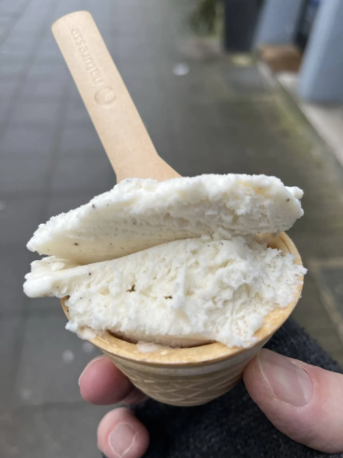 Ein kleiner essbarer Eisbecher mit Vanilleeis und einem Papplöffel.
