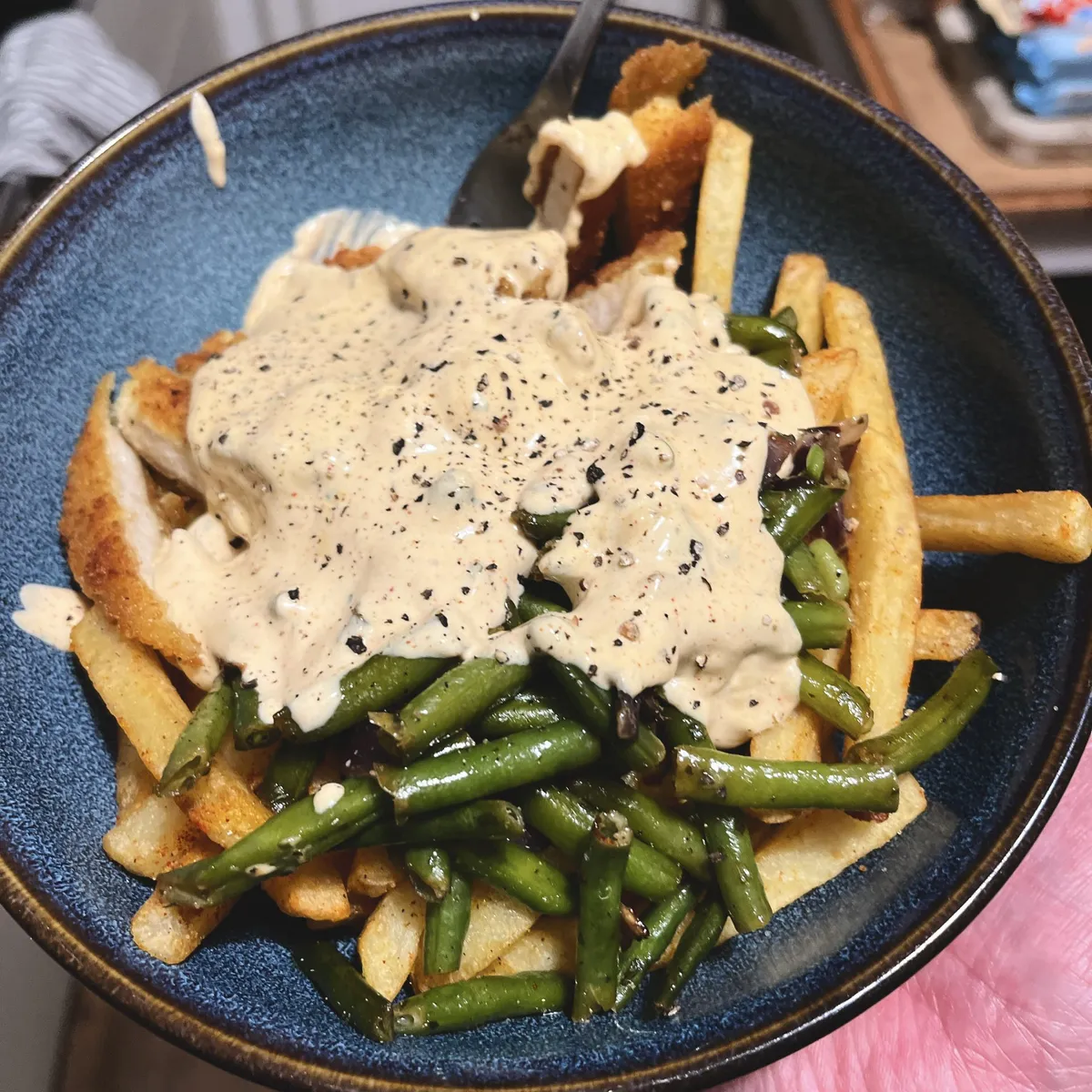 Ein Teller mit Pommes, Schnitzel, grünen Bohnen und Sauce Hollandaise.